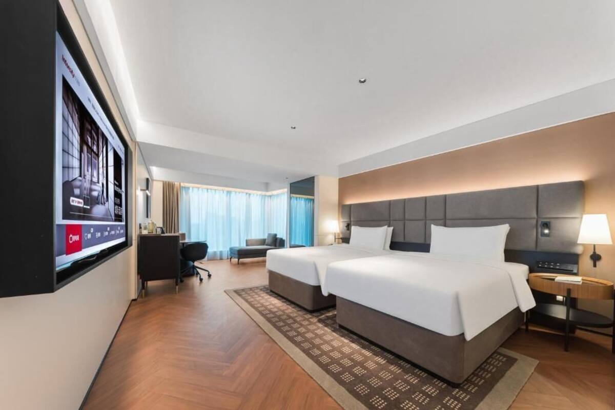 Hotelkamer met een groot bed, een bureau, een stoel, een aan de muur bevestigde televisie en een raam met gordijnen.