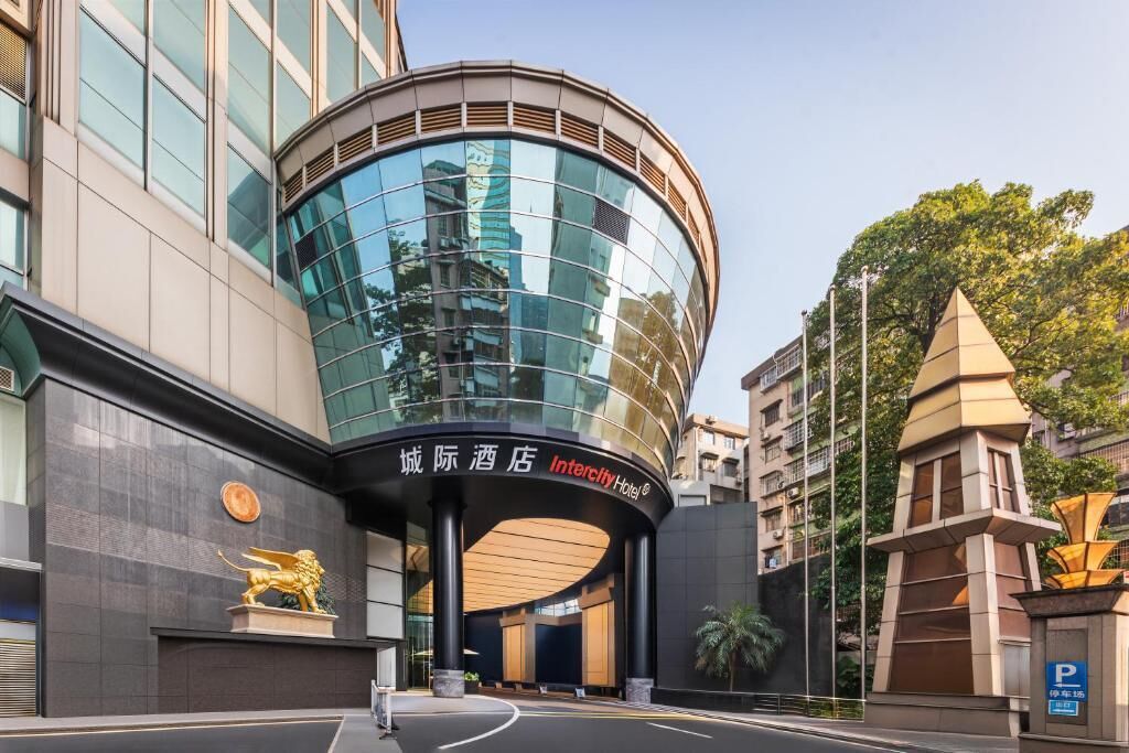 A modern hotel with a curved glass facade, a prominent lion statue, and a clear sky.