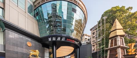 A modern hotel with a curved glass facade, a prominent lion statue, and a clear sky.