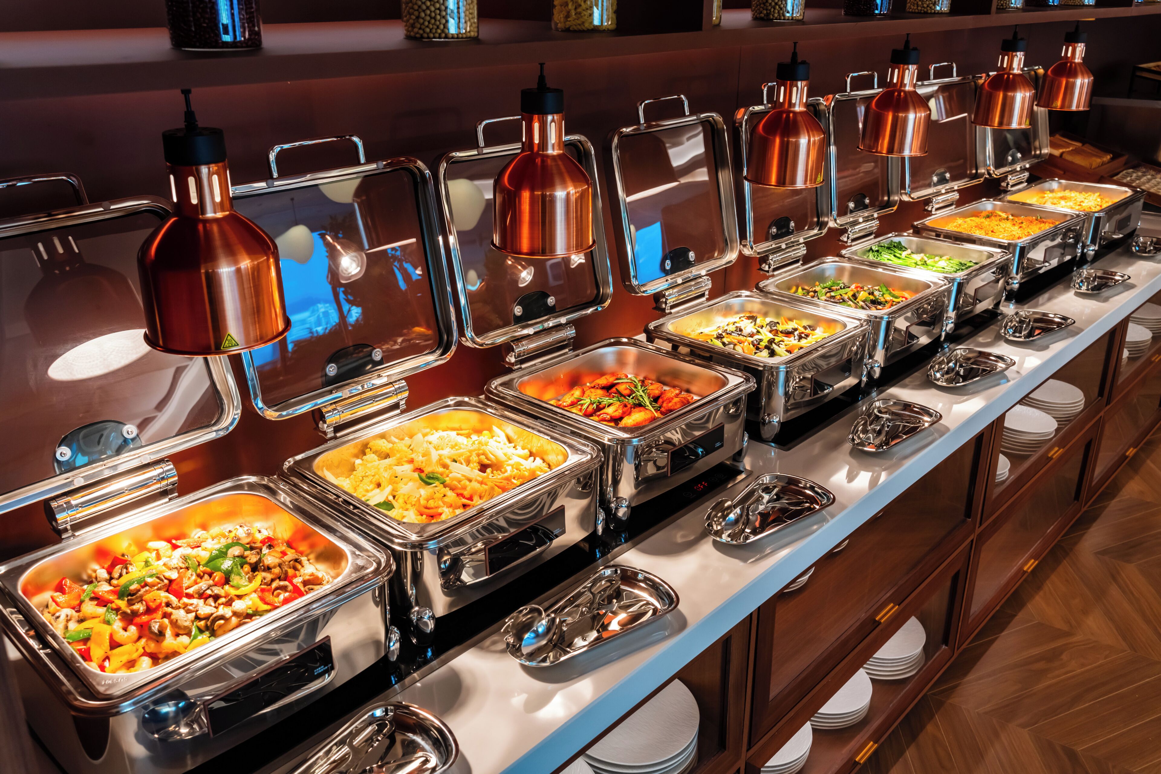 A buffet with multiple food stations, each with a metal container and a glass cover.
