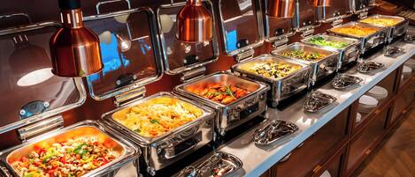 A buffet with multiple food stations, each with a metal container and a glass cover.