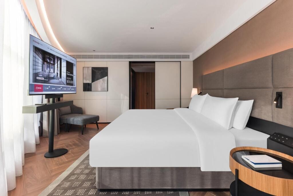 A modern hotel room with a large bed, a television, a desk, and a chair.