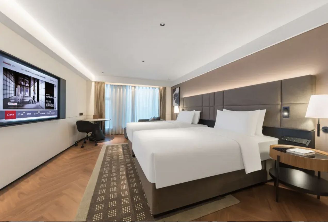 Una habitación de hotel con dos camas, televisión, escritorio y ventana con cortinas.
