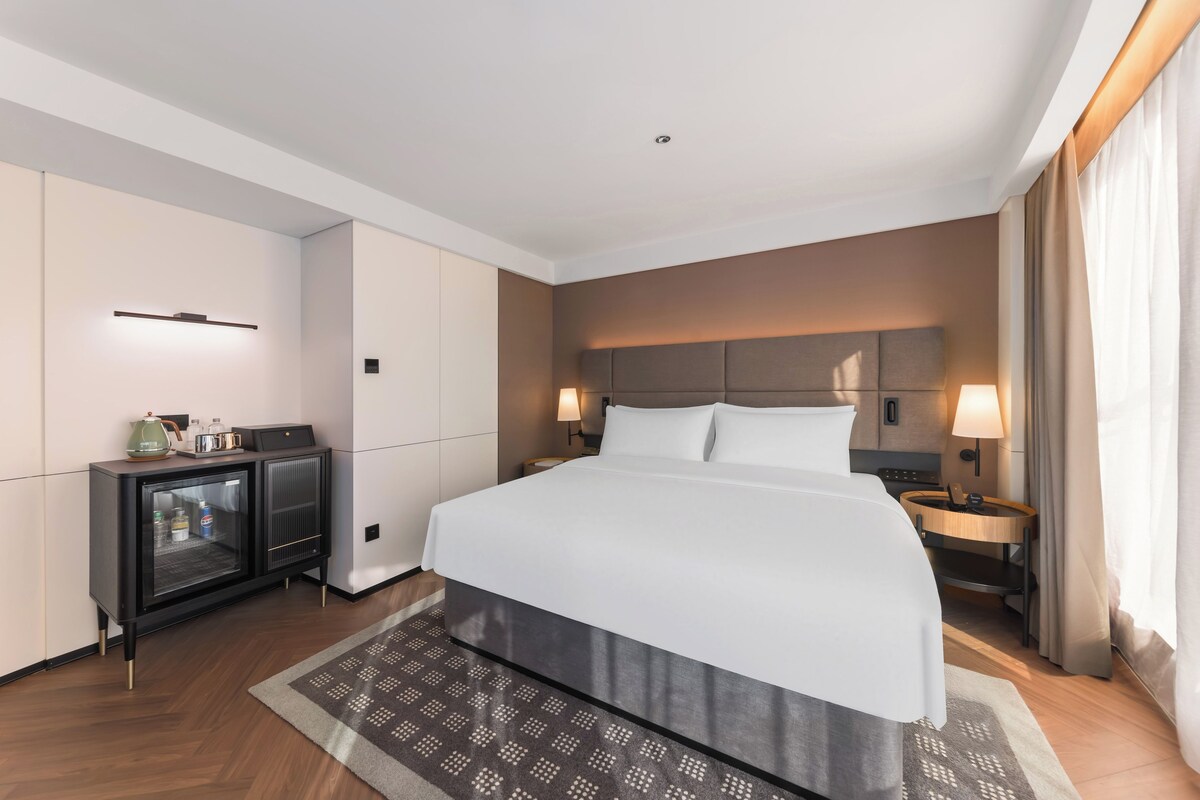 Une chambre d’hôtel moderne dotée d’un grand lit, de tables de chevet, d’un minibar et offrant une vue sur la ville.