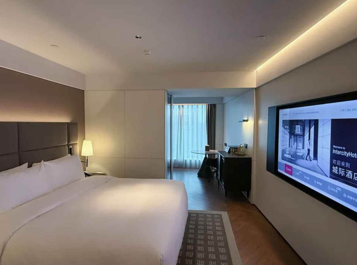 A hotel room with a large bed, a desk, and a television screen displaying a welcome message.