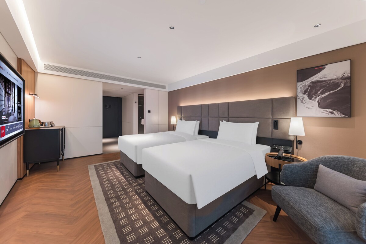 Ein Hotelzimmer mit zwei Betten, einem Fernseher, einem Schreibtisch, einer Couch und einem großen Gemälde an der Wand.