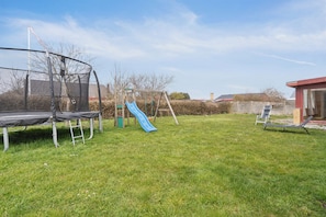 En baghave med trampolin, gyngestativ, rutschebane og en liggestol.