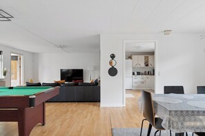 A modern living room with a pool table, a flat-screen TV, and a dining area with a table and chairs.