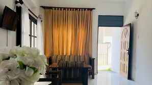 A hotel room with a dining table, a vase of flowers, a ceiling fan, a sofa, and a view of the outside.