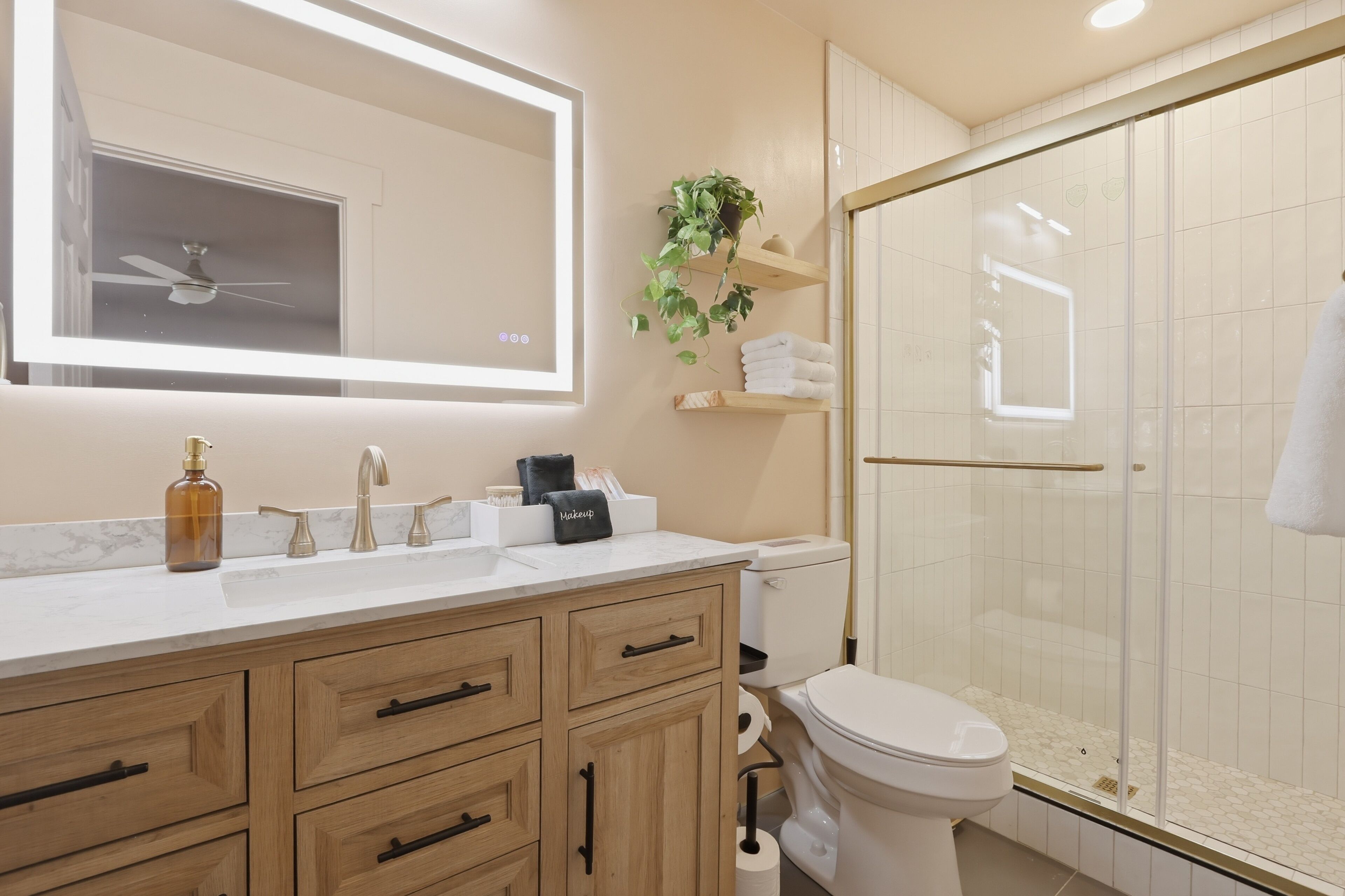 A modern bathroom with a vanity, a toilet, a shower enclosure, and a ceiling fan.