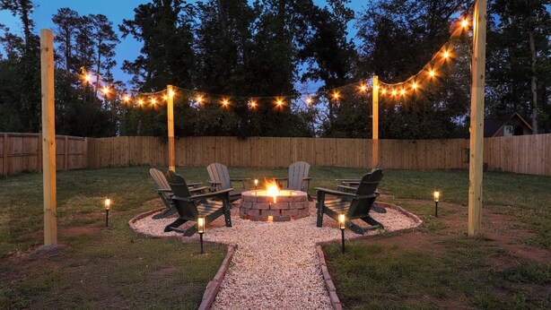 Ein Garten mit Feuerstelle, Sitzgelegenheiten und Lichterketten.