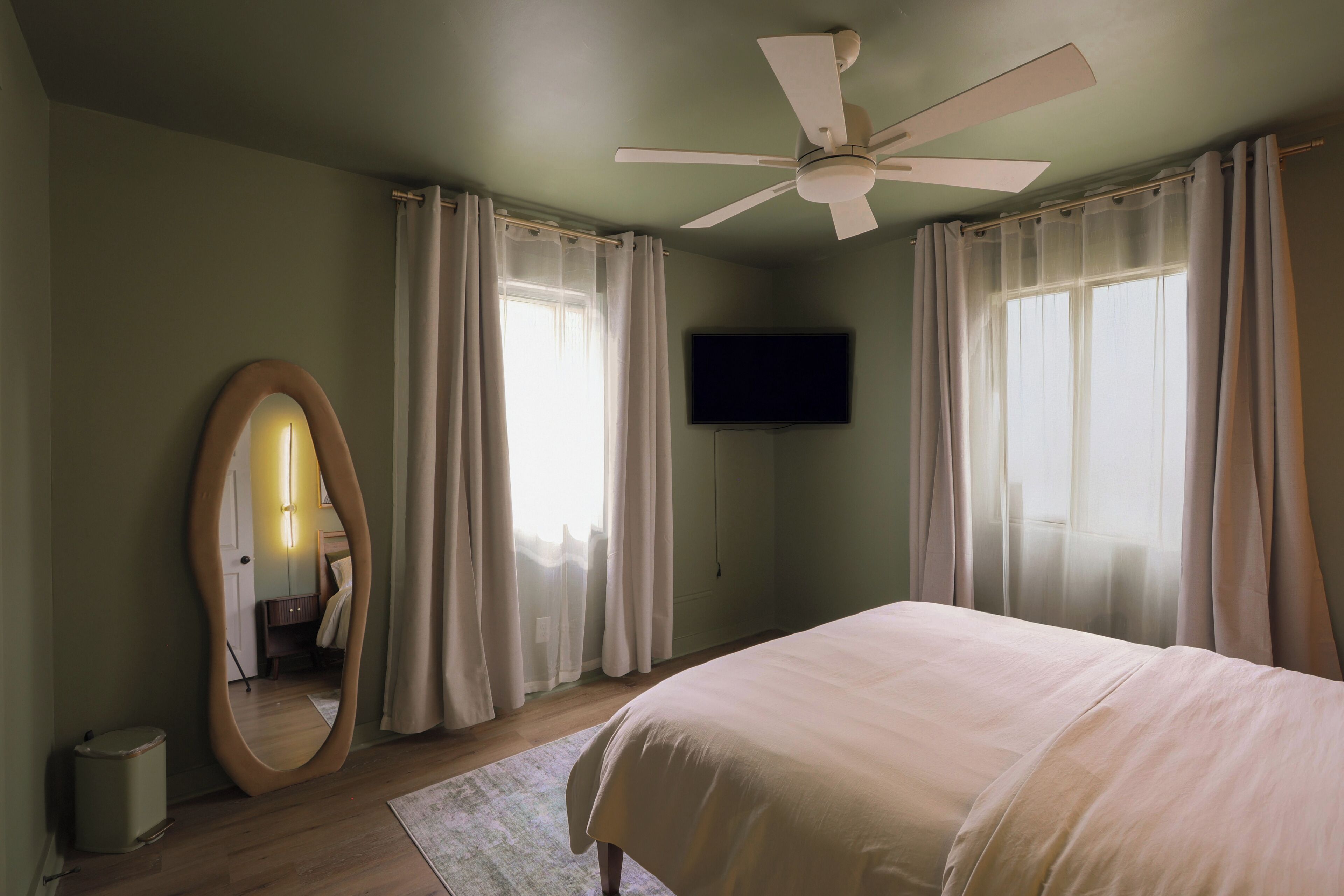 Une chambre à coucher avec un lit, un ventilateur de plafond, une télévision et un miroir.