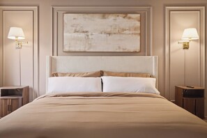Una cama bien hecha con cabecera, dos mesitas de noche y lámparas de pared.