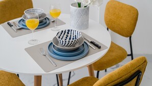 Ein runder Esstisch mit blauen und weißen Schalen, ein Glas Orangensaft und eine Vase mit weißen Blumen.