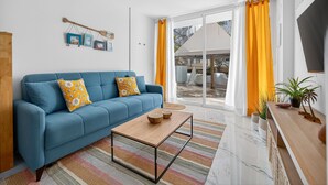 Ein modernes Wohnzimmer mit einem blauen Sofa, einem Holztisch und einem großen Fenster mit gelben Vorhängen.