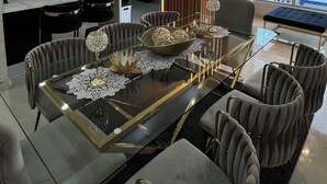 Un área de comedor moderna con una mesa de vidrio, sillas tapizadas y vistas de la ciudad a través de amplios ventanales.