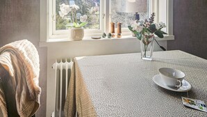 A room with a radiator, a window with white curtains, a table with a patterned tablecloth, a vase with flowers, and a cup on the table. - 1 bedroom stunning apartment in Vimmerby (Vimmerby)