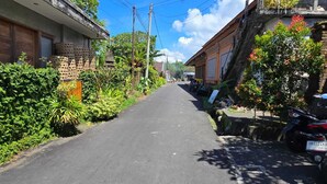 A narrow street lined with residential buildings, a parked motorcycle, and lush greenery. - Kami House Ubud (Ubud)