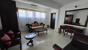 A living room with a sofa, a round coffee table, a wooden chair, a small table, and a mirror on the wall. - Kami House Ubud (Ubud)