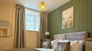 Una camera da letto con un letto, una finestra con tende, una lampada, un quadro appeso al muro e un lampadario.