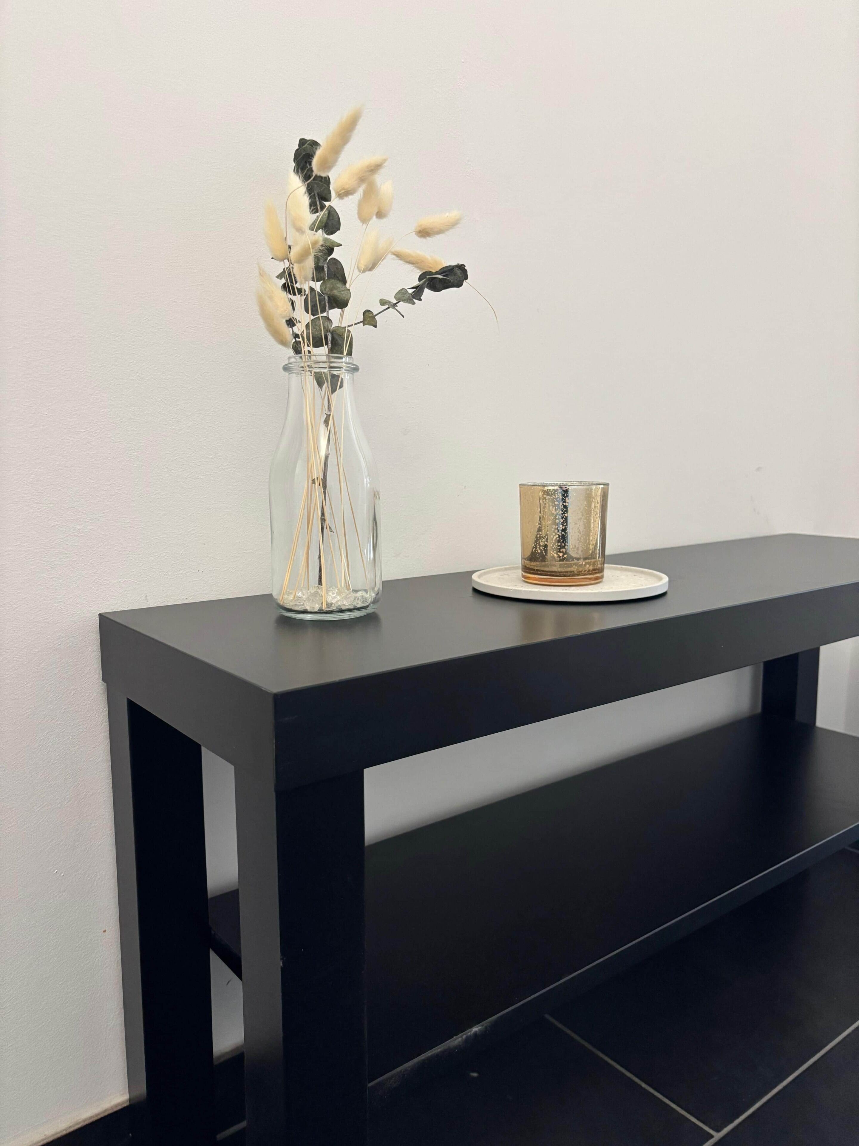 A black table with a clear glass vase containing dried plants and a small glass.