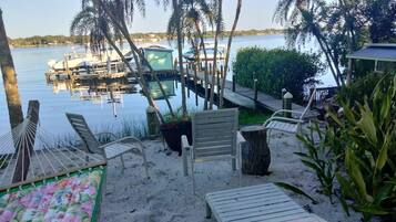 Un espace aménagé au bord de la plage, avec des chaises longues, un hamac et une vue sur les bateaux amarrés dans une marina.