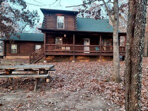 A rustic log cabin with a porch, a staircase, and a picnic table.