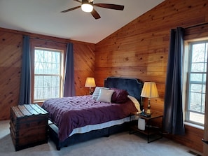 Une chambre à coucher aux murs lambrés, avec un lit, deux lampes de chevet, un ventilateur de plafond et une fenêtre.