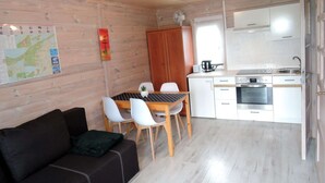 Une pièce de taille modeste avec un plafond en bois, une table à manger avec des chaises, un coin cuisine équipé d’une cuisinière et d’un évier, et une carte accrochée au mur.