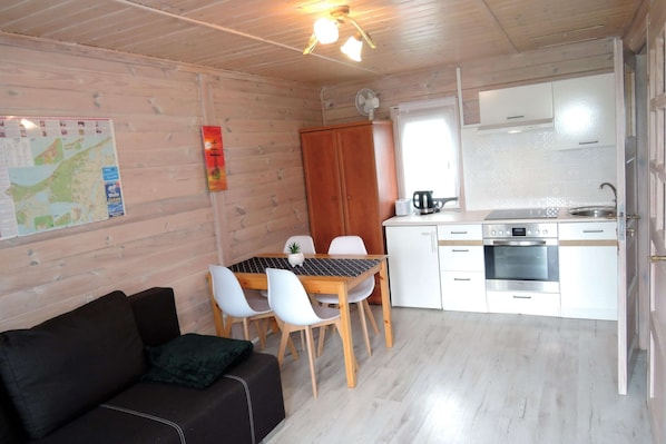 A compact room with a wooden ceiling, a dining table with chairs, a kitchenette with a stove and sink, and a map on the wall. - Holiday Home in Kolczewo Near Baltic Sea (gmina Wolin)