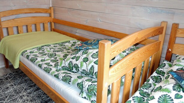 Un lit en bois avec une couvre-lit à motifs de feuilles, un plaid vert et une tête de lit en bois.