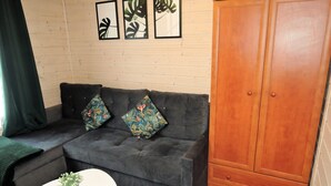 Un canapé gris agrémenté de coussins à motifs floraux, une table basse blanche avec une plante, et une armoire en bois.