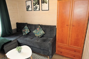 A grey sofa with floral cushions, a white coffee table with a plant, and a wooden wardrobe. - Holiday Home in Kolczewo Near Baltic Sea (gmina Wolin)