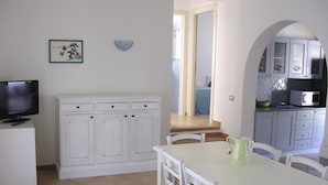 Een kleine keuken met witte kasten, een eettafel en een televisie op een standaard.