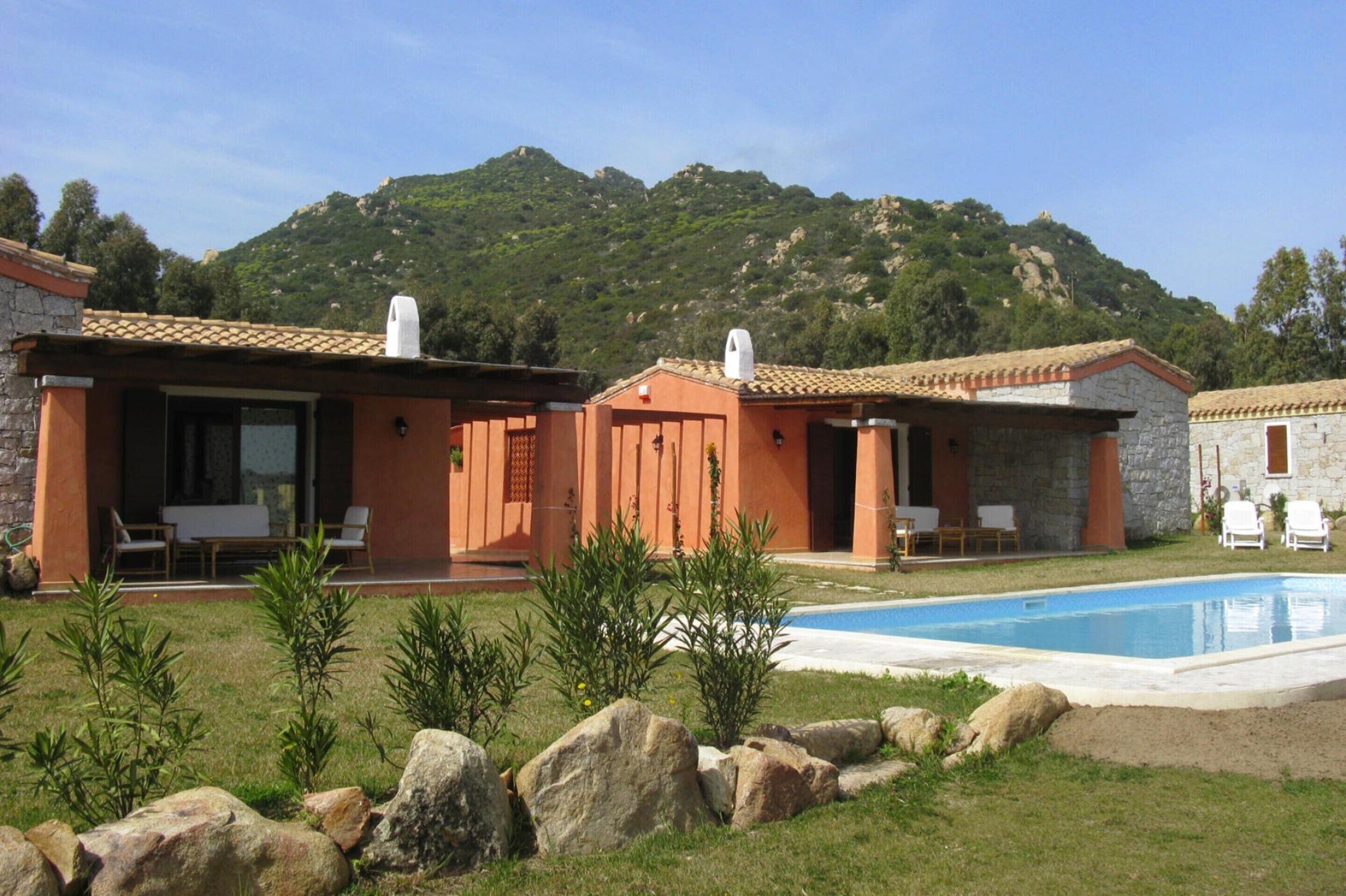 A villa with a swimming pool, outdoor seating, and a mountainous backdrop.