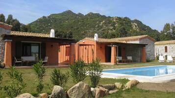 A two-story building with a swimming pool, outdoor seating, and a mountainous backdrop.
