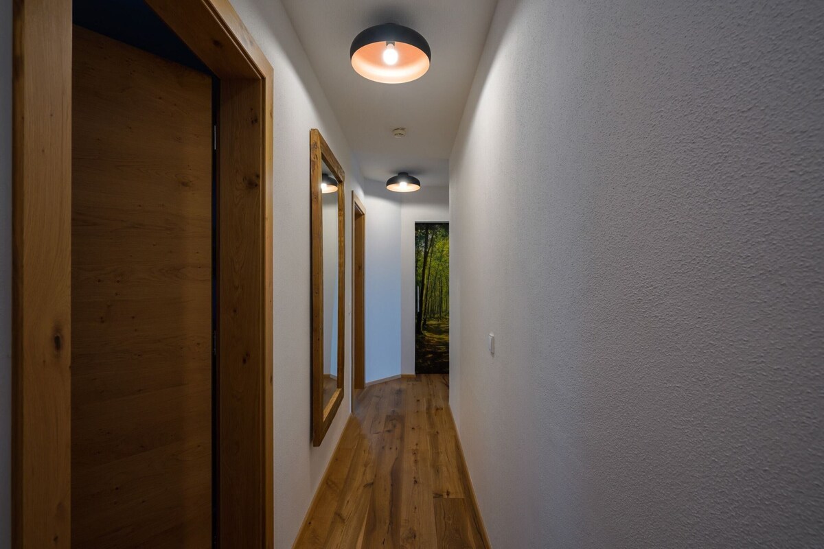 A hallway with wooden flooring, white walls, and a ceiling light fixture.
