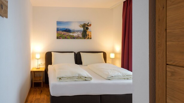 Un lit bien fait, avec du linge de lit blanc, deux lampes de chevet, une petite table de chevet et un tableau représentant un paysage accroché au mur.