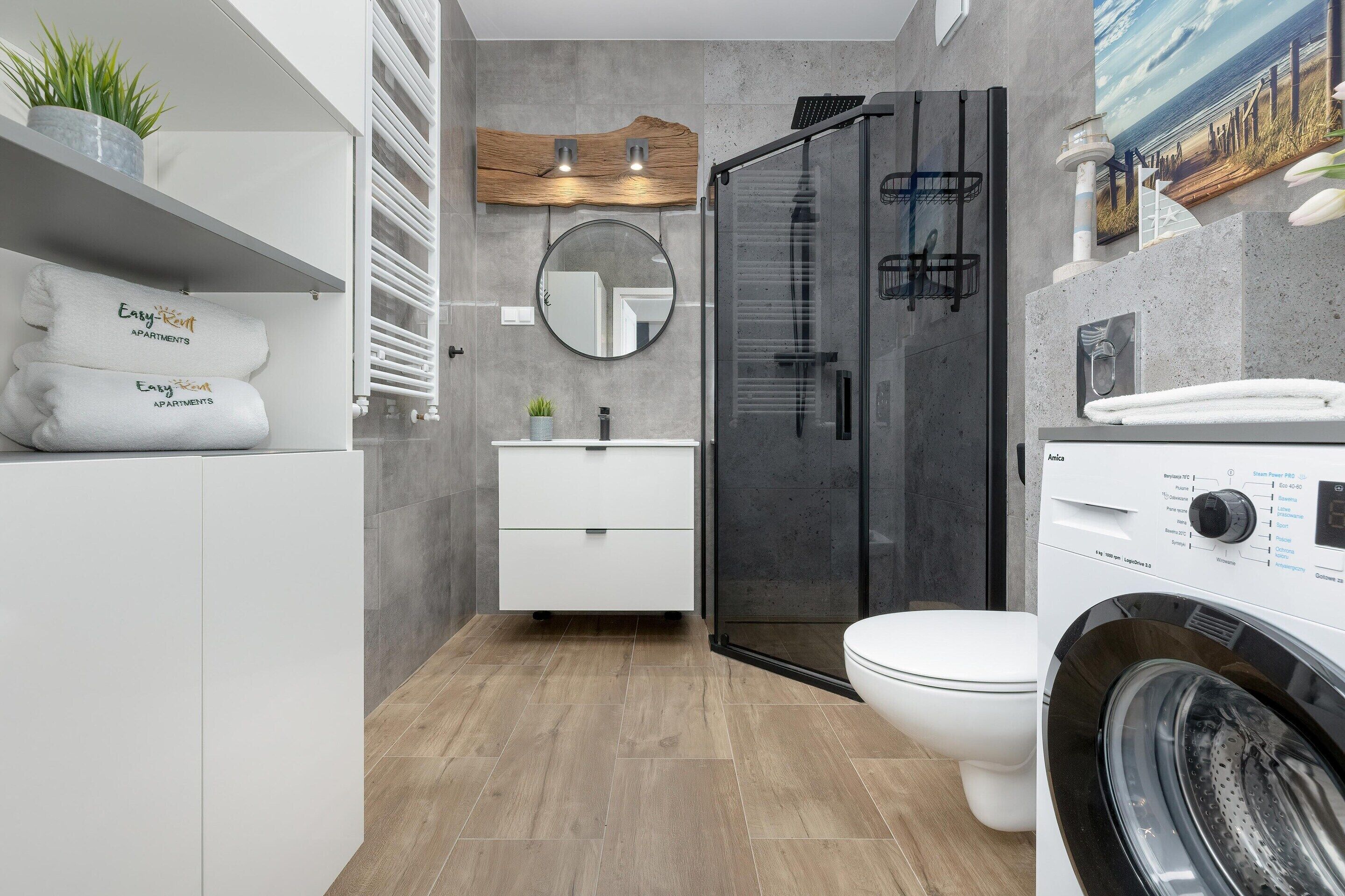 Un baño moderno con cabina de ducha de vidrio, un lavabo blanco y una lavadora integrada.