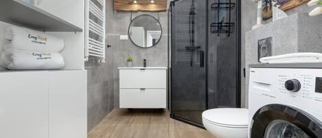 Un baño moderno con cabina de ducha de vidrio, un lavabo blanco y una lavadora integrada.