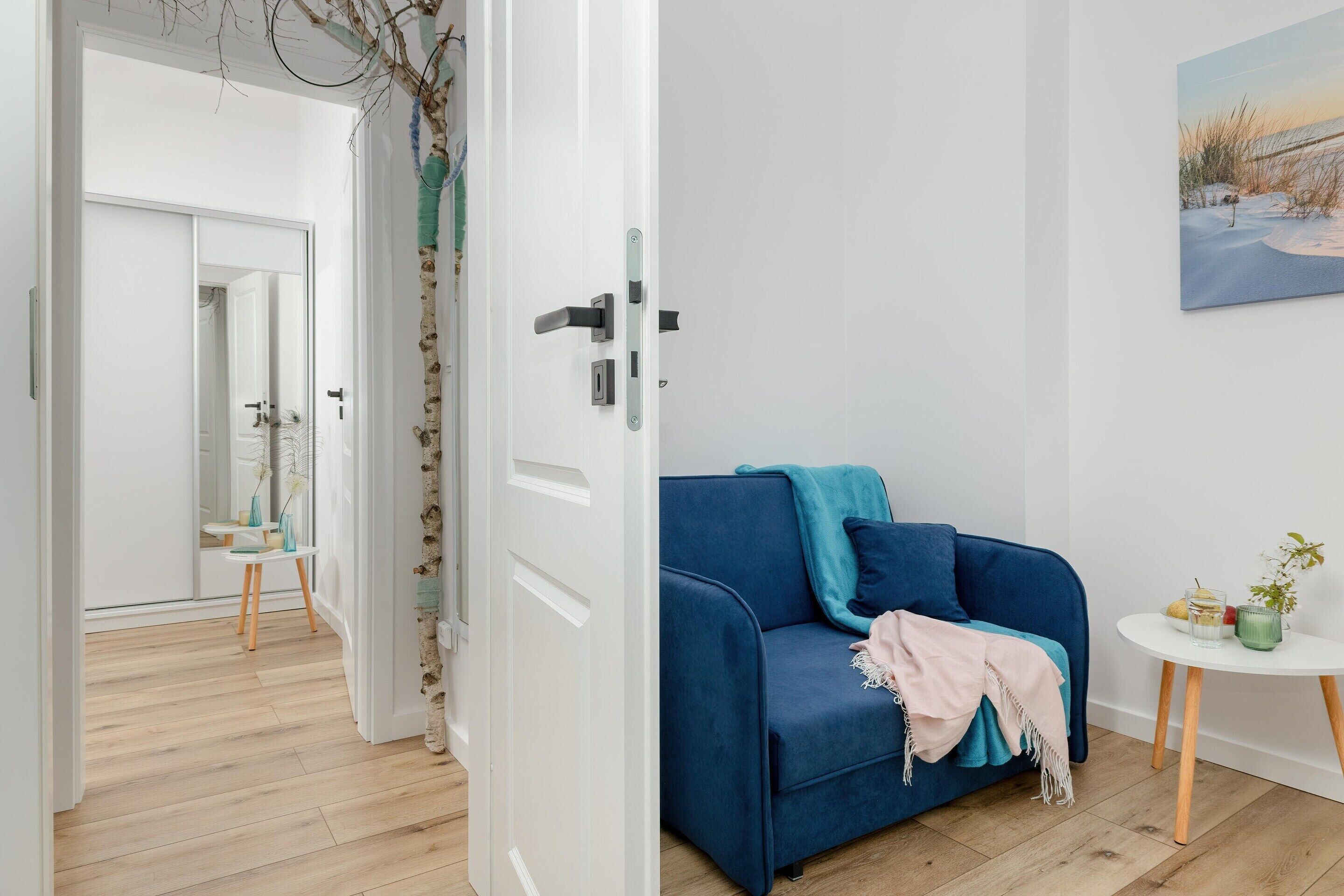 A room with a blue sofa, a small white table, and a painting on the wall.