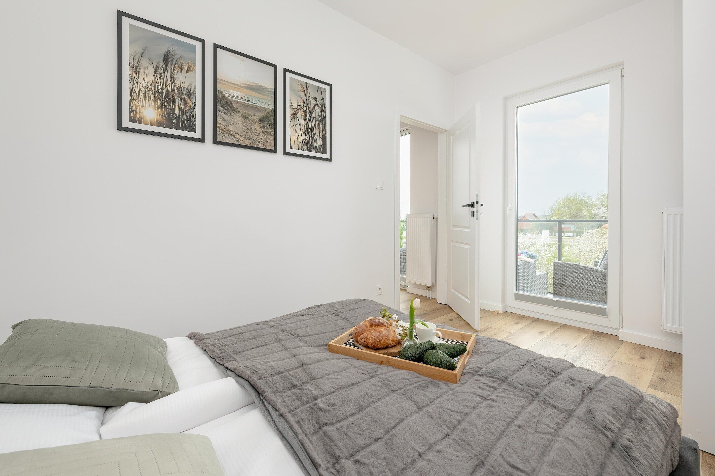 Ein Schlafzimmer mit einem Bett, einer grauen Steudecke, einem Tablett mit Speisen und Blick auf einen Balkon.