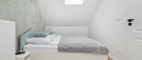 A compact, modern bedroom with a skylight, a built-in bed, a bedside table, and a radiator.
