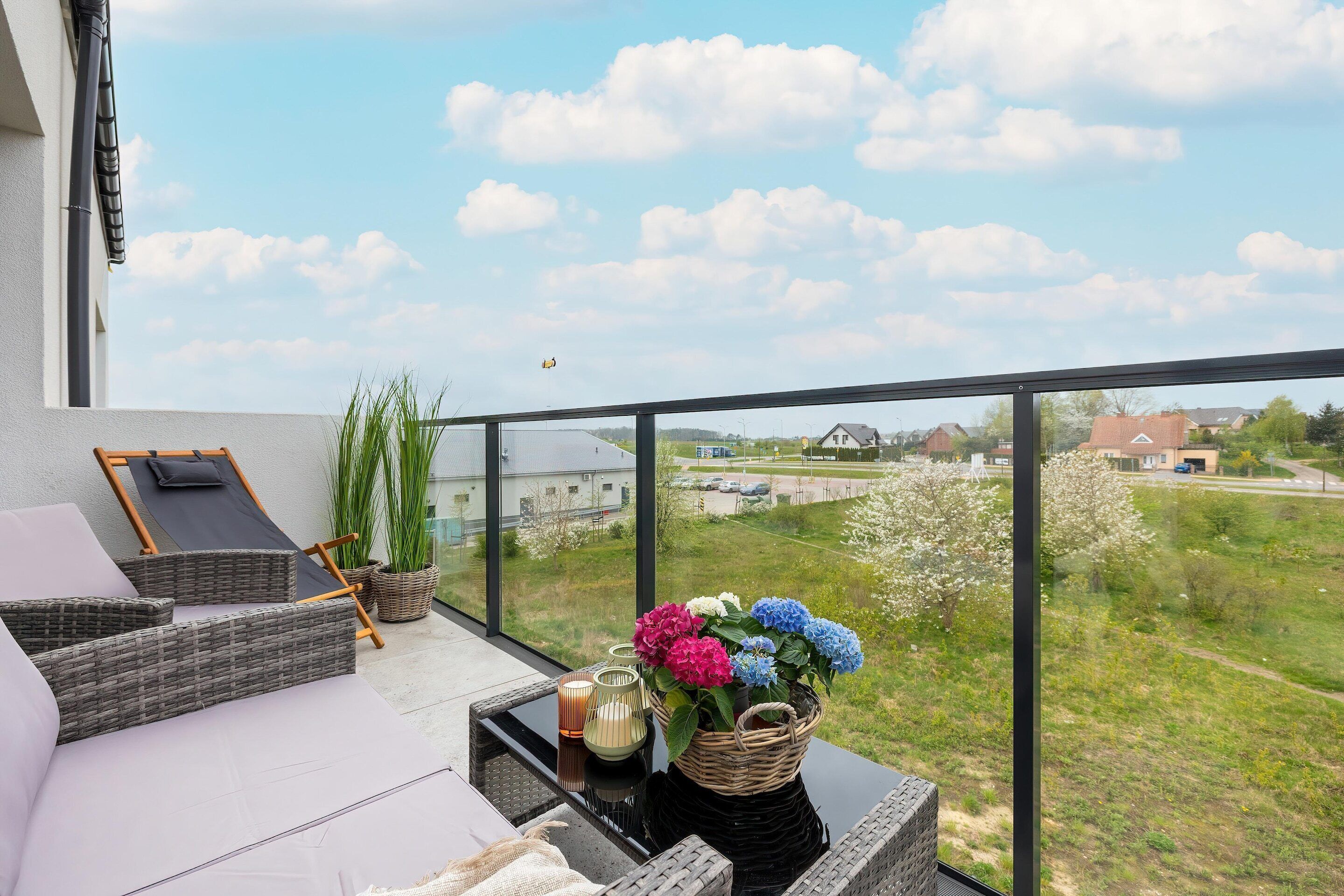 A balcony with wicker furniture, a wicker basket with flowers, and a view of a green landscape.