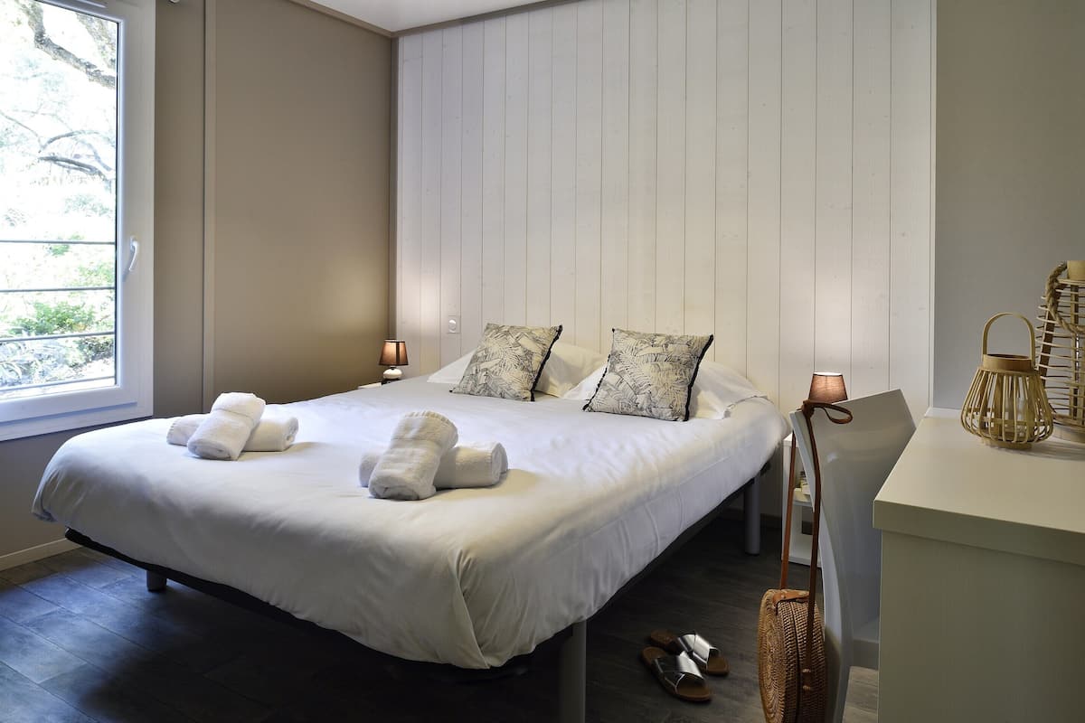 A neatly made bed with towels, a bedside table with a lamp, and a window with a view.
