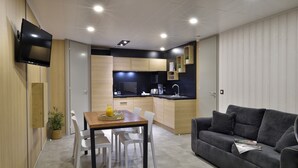 A modern kitchen with a dining area, a grey sofa, and a flat-screen TV mounted on the wall. - Group Stay Near Sea in Propriano (Belvedere-Campomoro)