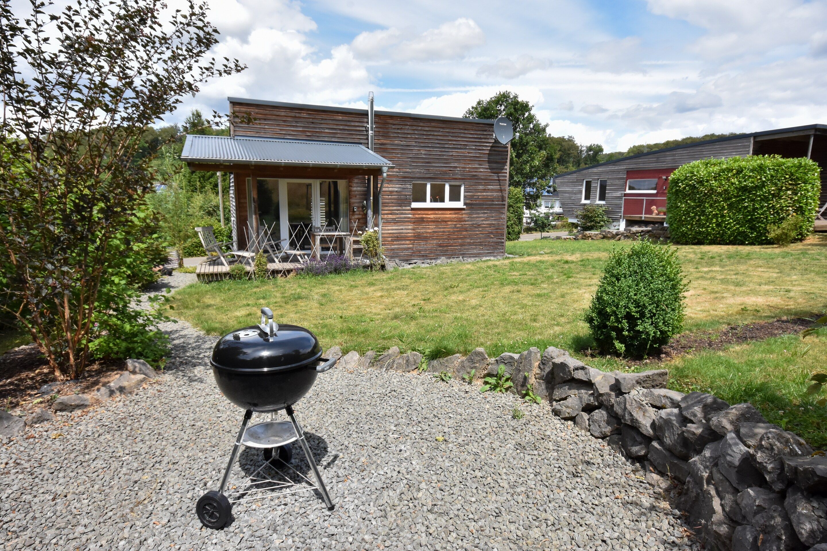 A modern house with a patio, a barbecue grill, and a stone wall.