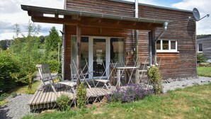 Ein modernes Holzhaus mit überdachter Terrasse, Sitzgelegenheit im Freien und einer Sat-Anlage.
