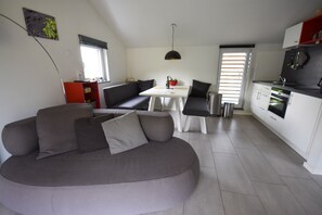 A modern living space with a grey sofa, a dining table, and a kitchen area. - Holiday Home in Forest With Terrace & BBQ (Berlingen)