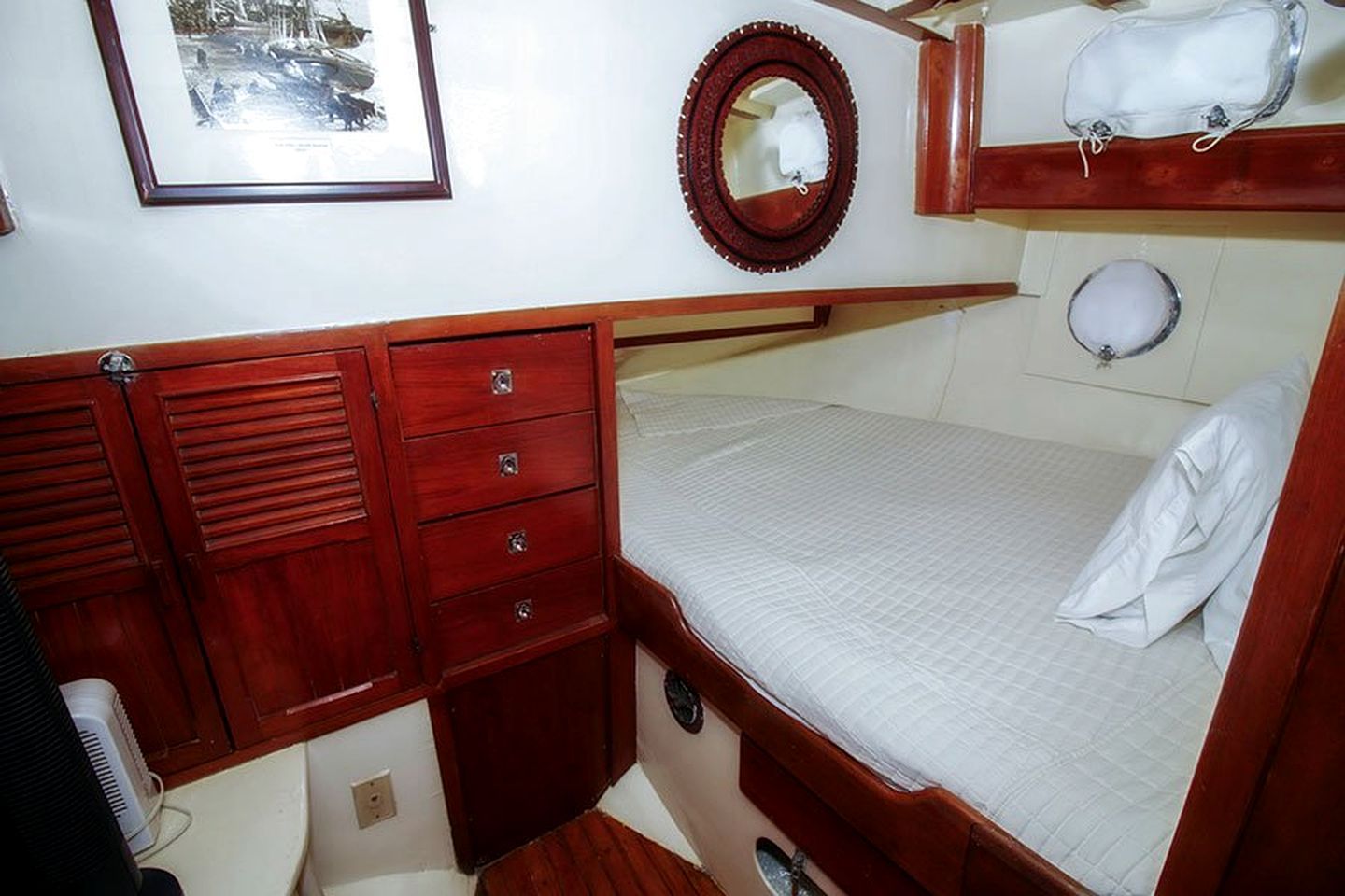 Una cabaña acogedora con una cama alta, un pequeño aparador de madera con cajones, un espejo y un cuadro en la pared.